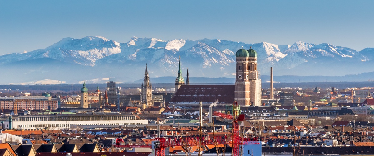 München Panorama mit Frauenkirche, schneebedeckten Alpen im Hintergrund und blauem Himmel